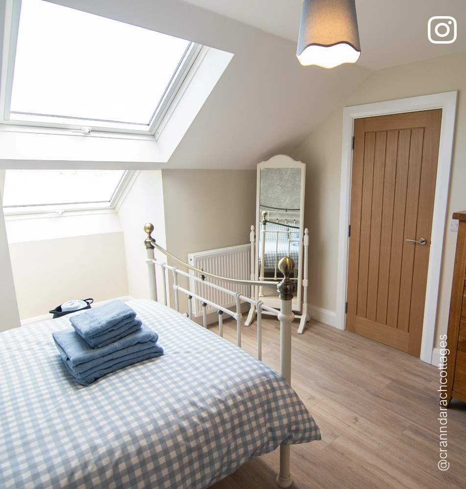 Bright attic bedroom at Crann Darach Cottages featuring a vintage iron bed, skylight window, and coastal-inspired décor near Benone Beach.