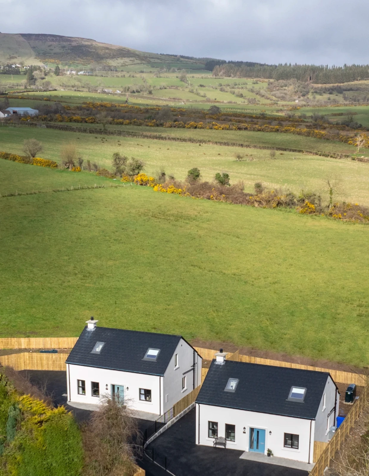 Aerial view of Crann Darach Cottages with rolling green fields and Binevenagh Mountain in the background, near Benone Beach, Northern Ireland.